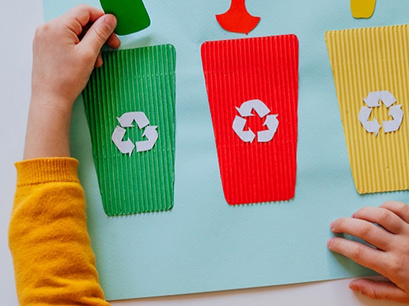 Enfant en train de jouer avec une activité manuelle représentant le tri des déchets, avec trois poubelles colorées (verte, rouge et jaune) portant le symbole du recyclage.
