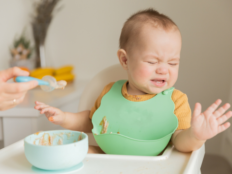 Un bébé détourne la tête en repoussant une cuillère, refusant de manger le plat proposé – illustration d’un comportement de néophobie alimentaire.
